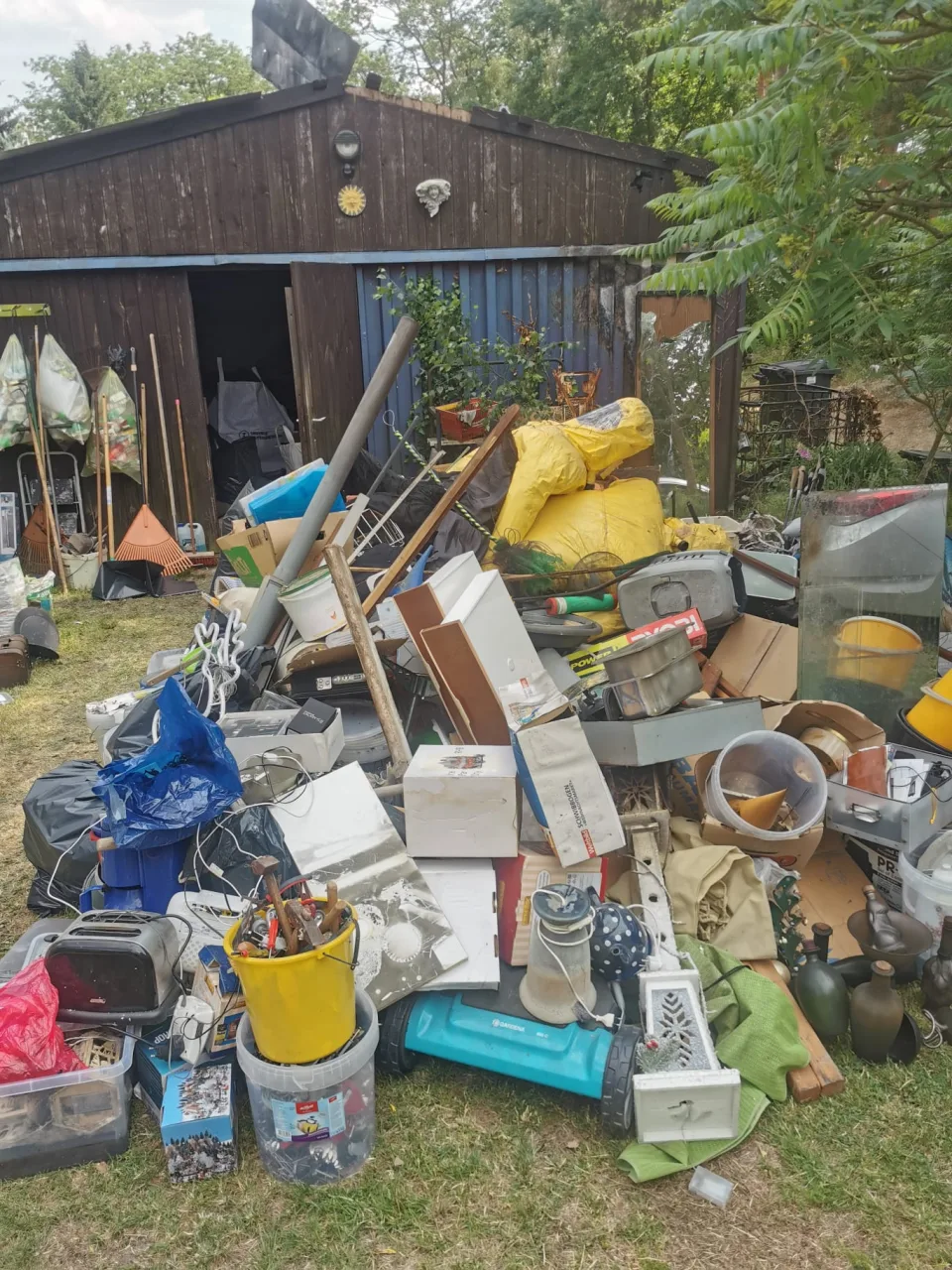 Zusammengetragenes Räumgut mit Möbelteilen und Haushaltsgegenständen vor einem Gartenschuppen