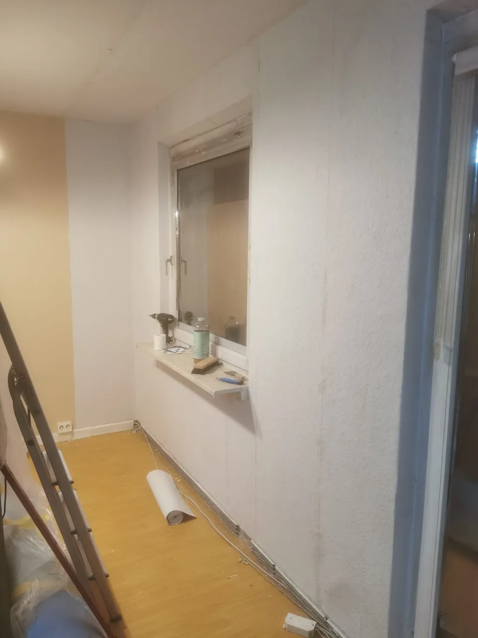 Bearbeitete Wandfläche an der Fensterfront mit Leiter und Tapezierwerkzeug
